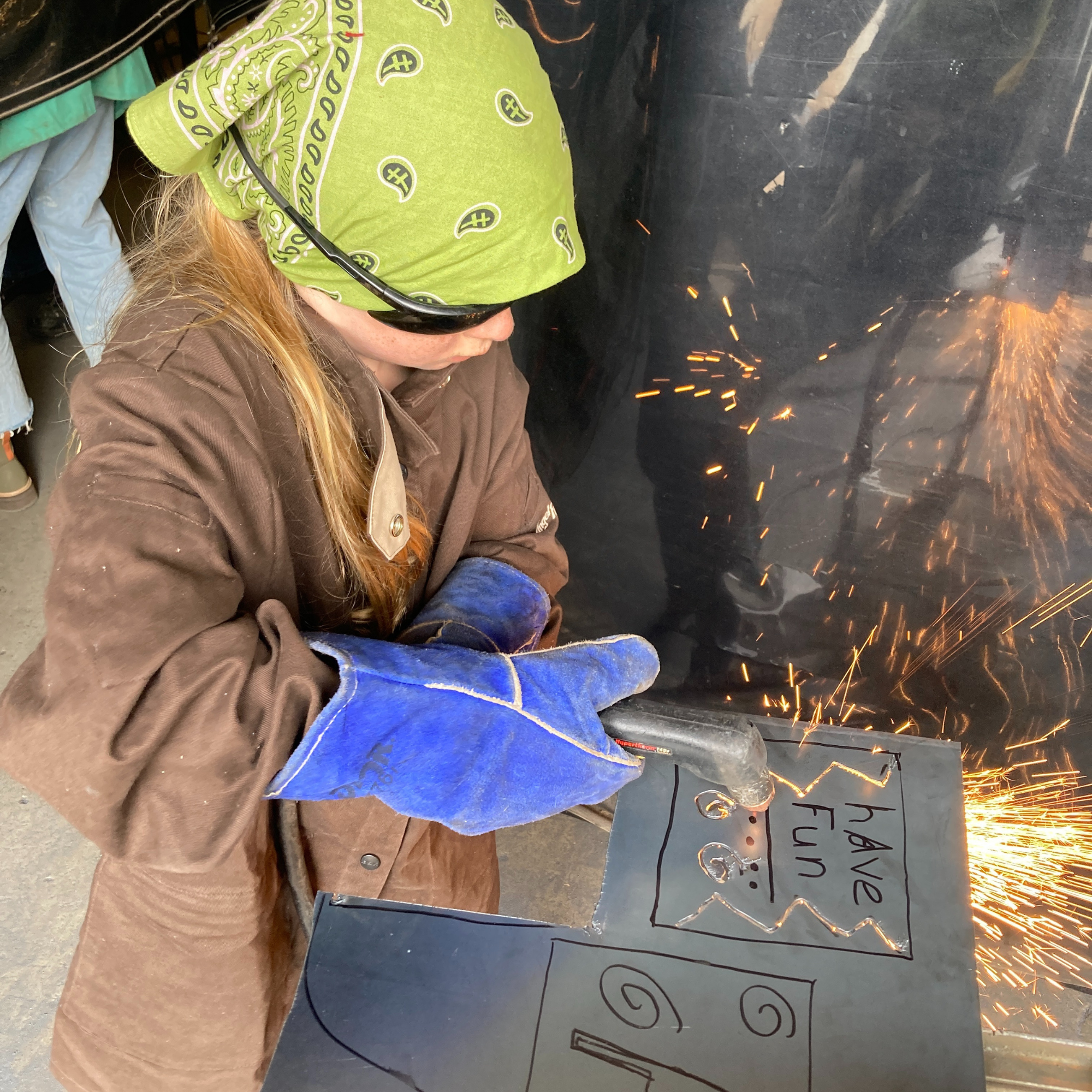 A middle school girl at Rosie's Girls WELD summer camp uses a plasma cutter to cut sheet metal