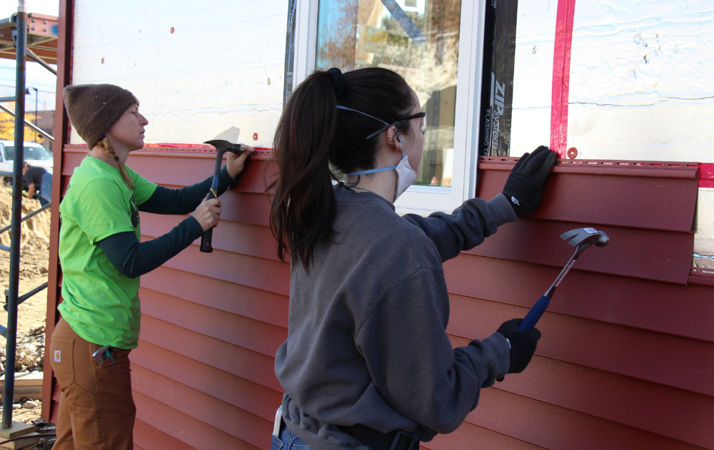 Trailblazers use a hammer to install siding on a house.