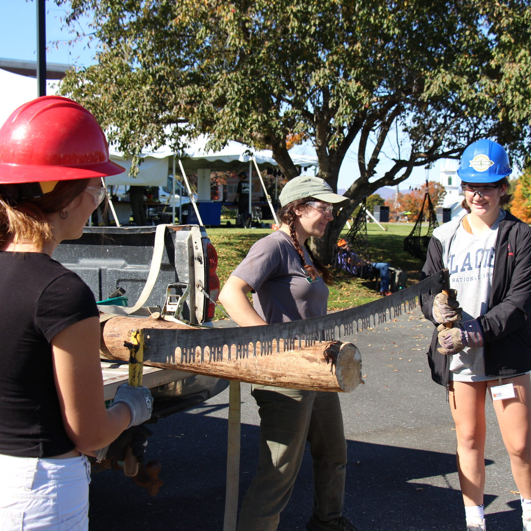 Two female high school students use a two-man crosscut saw under the supervision of a Green Mountain Club employee at Women Can Do 2022.