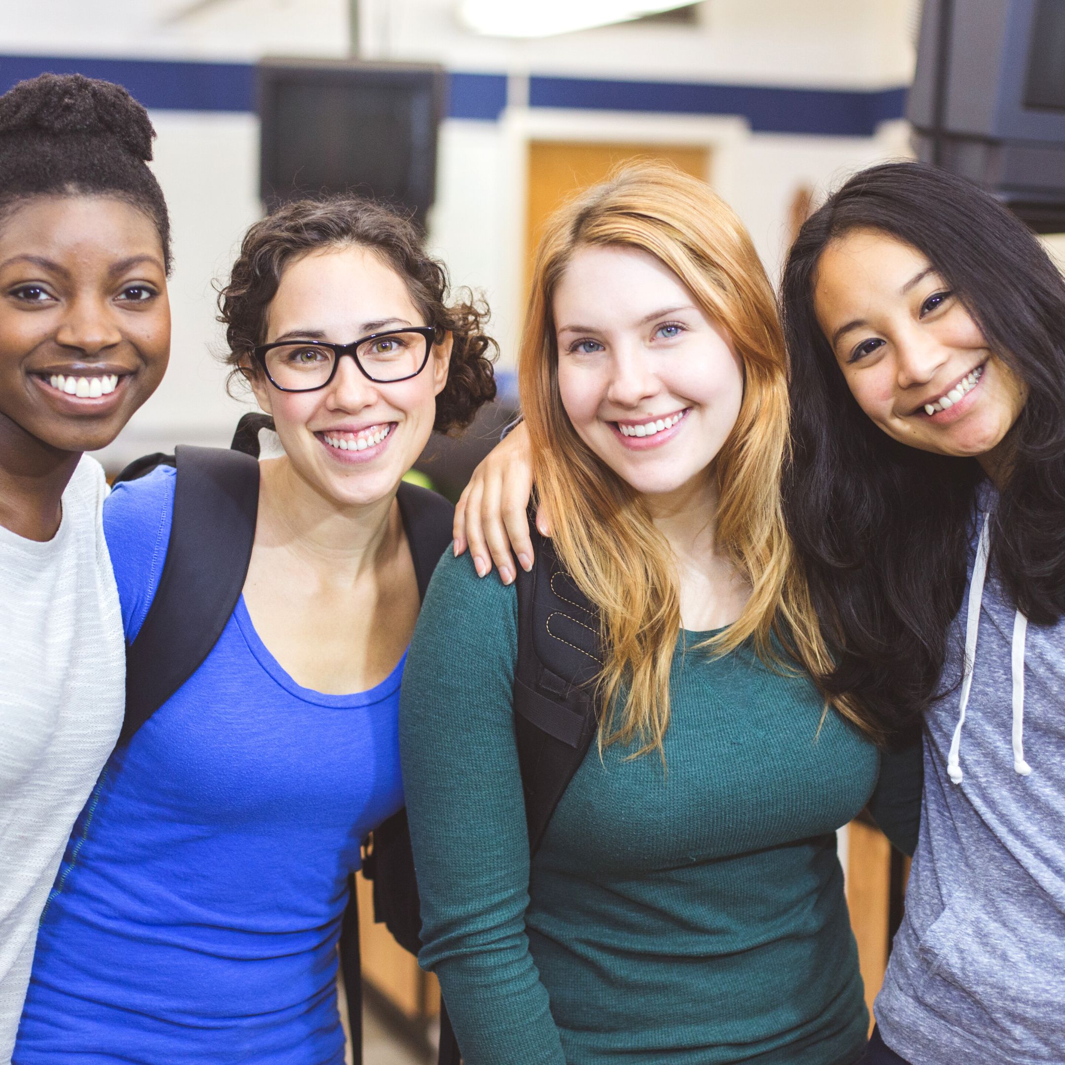 A group of young women wearing backpacks stand together, posing for a photo. High school students can participate in Youth@Work.