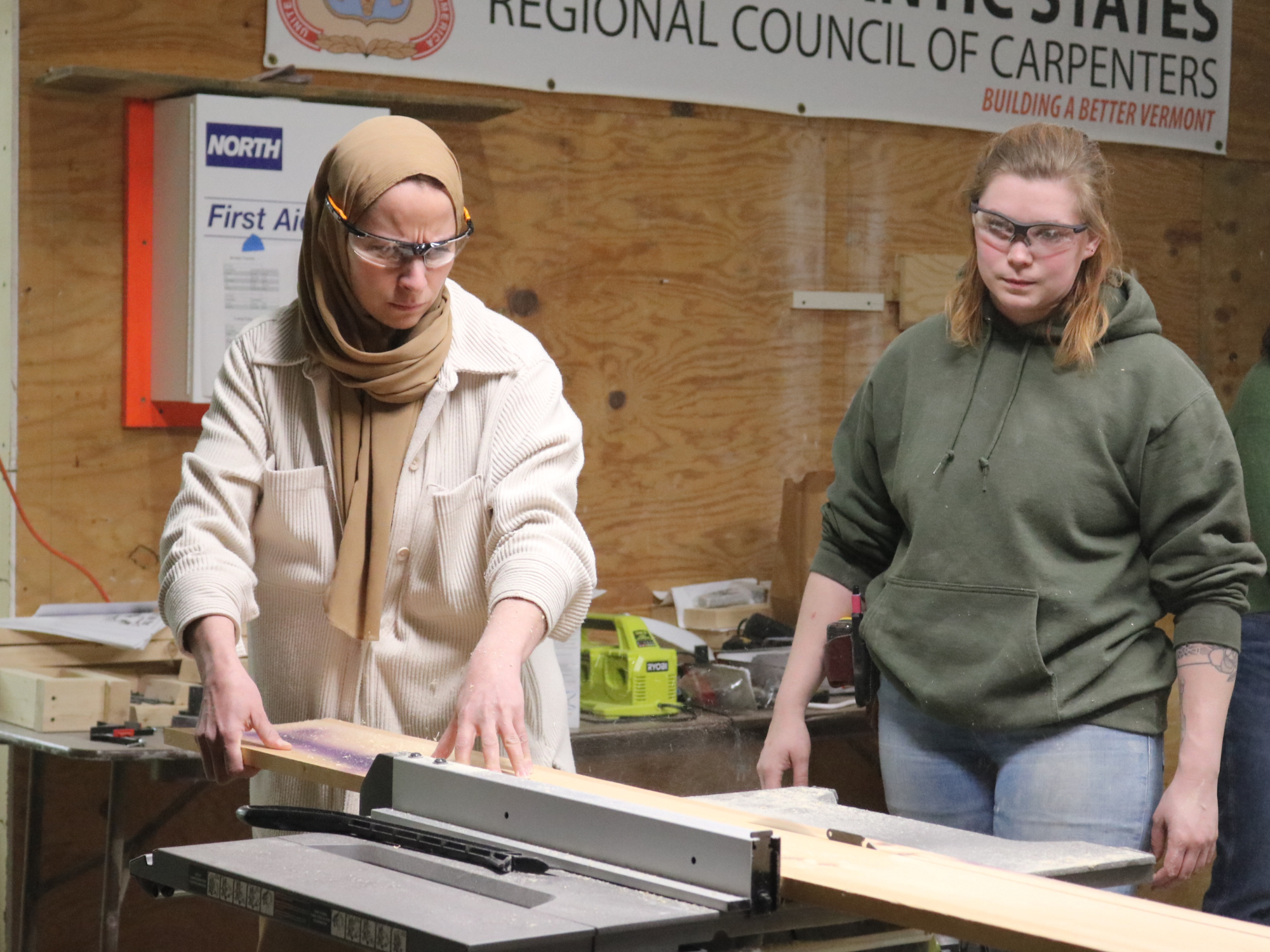 Participant uses a table saw to cut wood while an instructor looks on at VWW's Trailblazers trades training program