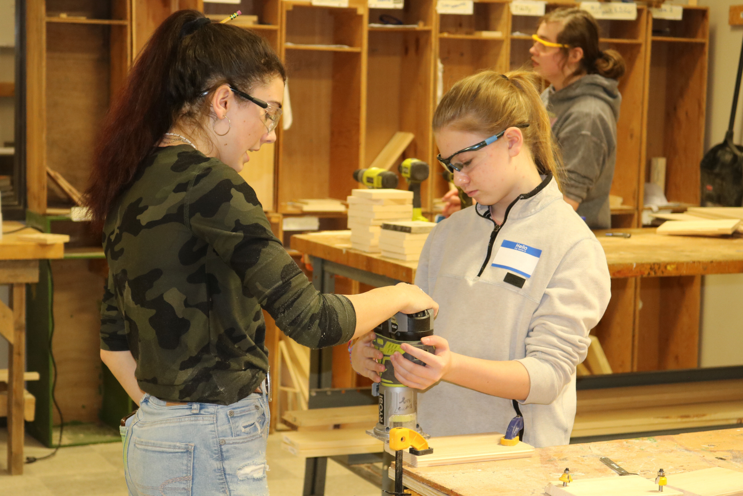 A current tech center student shows a middle school girl how to use a sander.