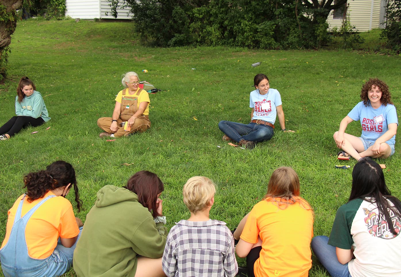 Vermont Works for Women staff and campers sit in a circle on the grass during Rosie's Girls summer camp.