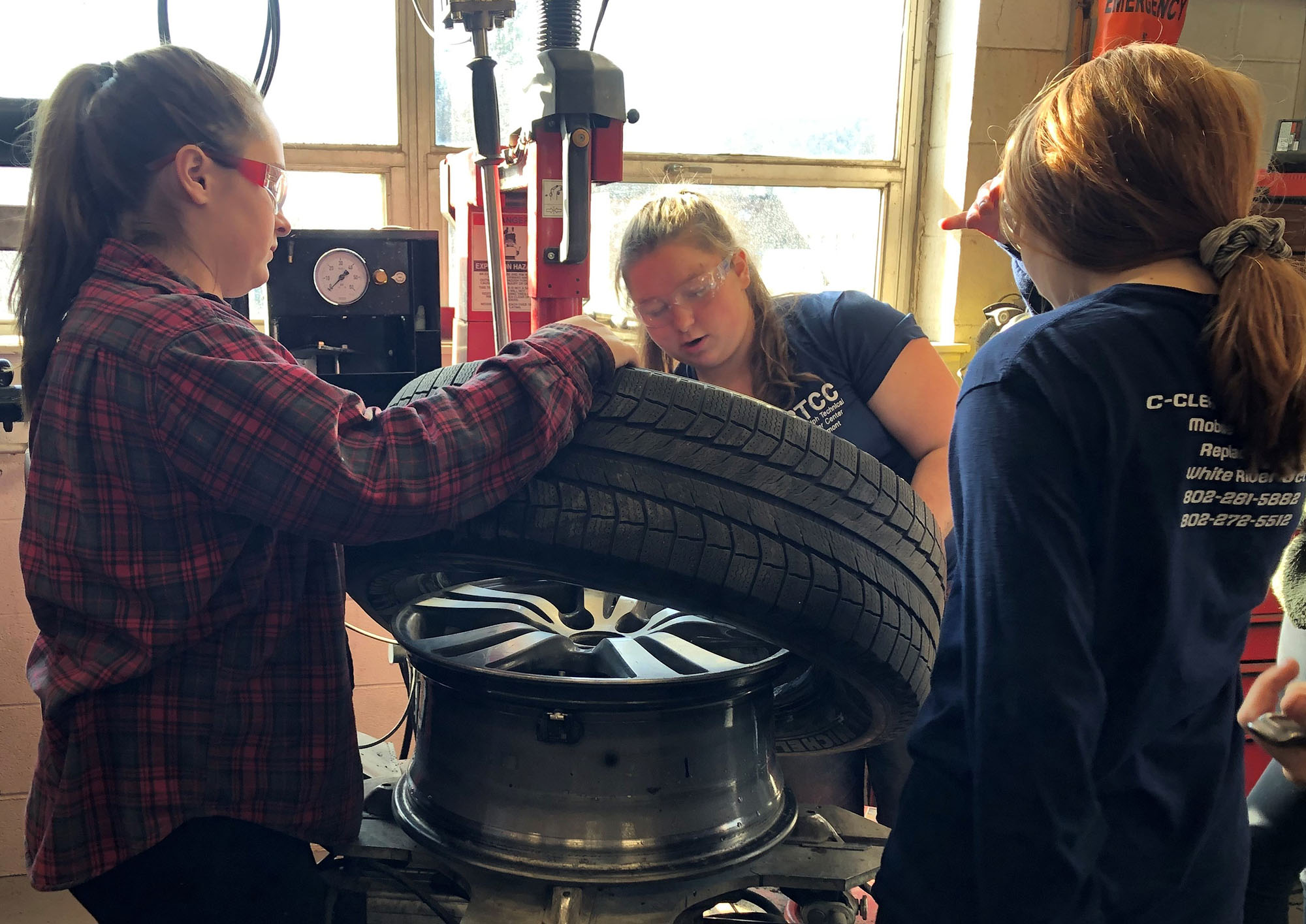 Female students demonstrate how to rotate a tire using a machine at Career Challenge Day.