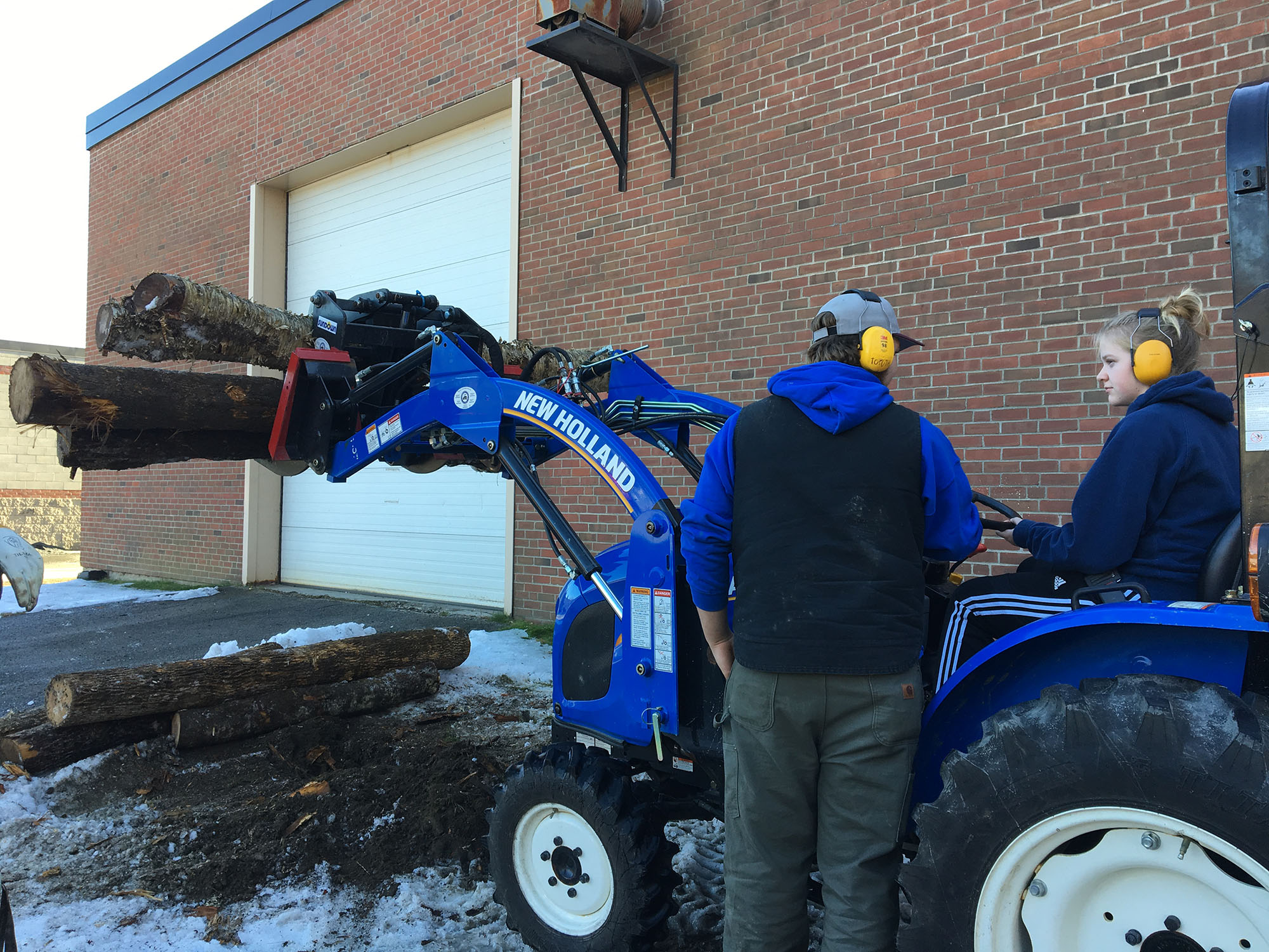 Teacher shows student how to lift timber logs using a front-loading tractor at Career Challenge Day.
