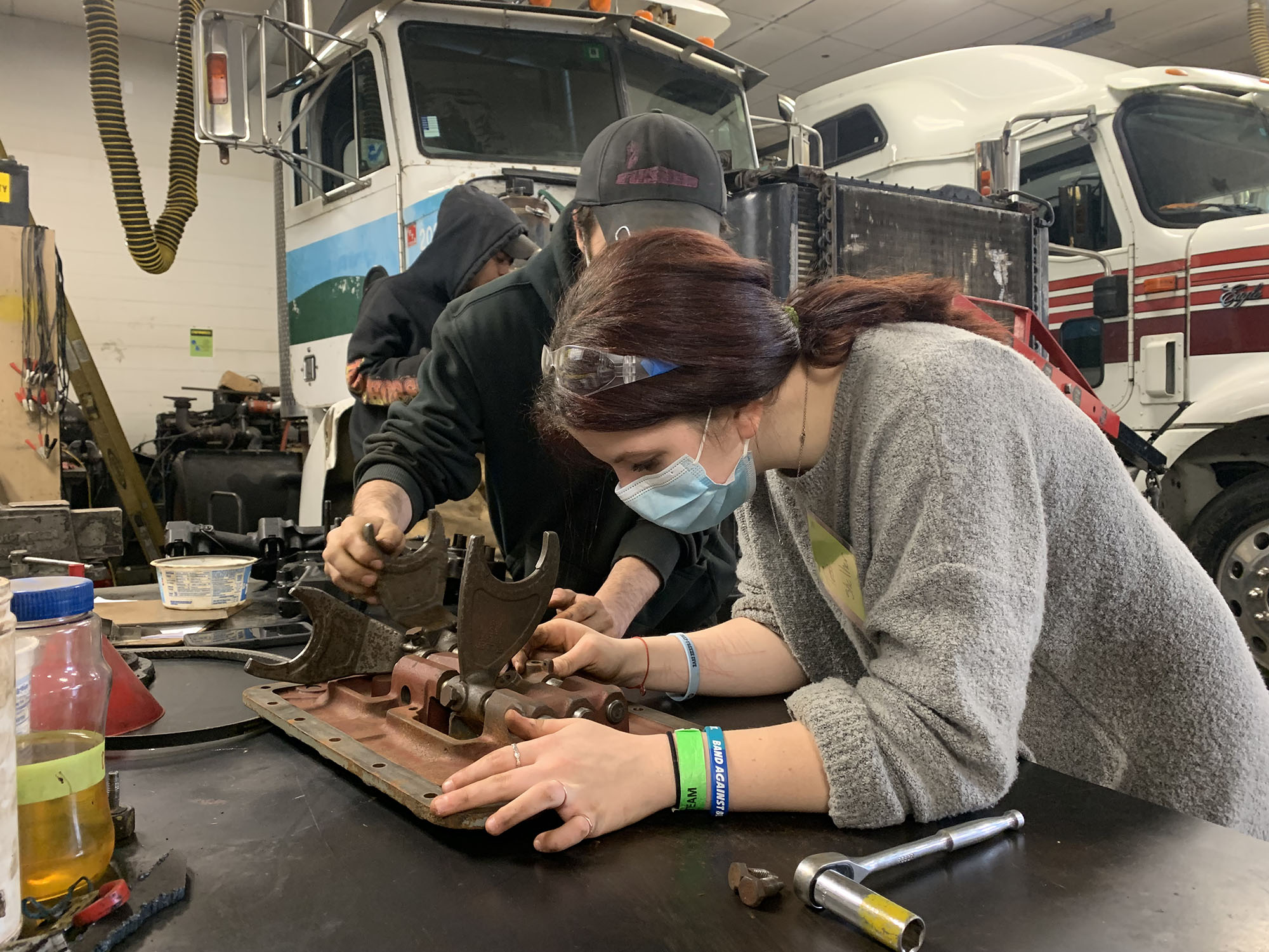 Female student investigates a metal car part on a table at Career Challenge Day.