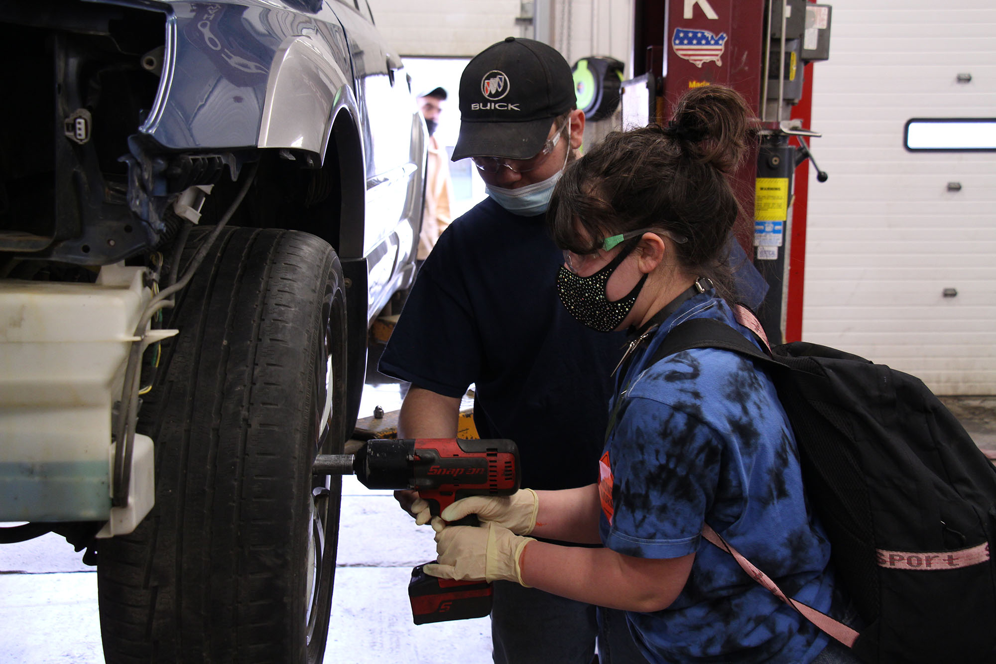 Female students use drill to remove lug nuts from a car at Career Challenge Day.