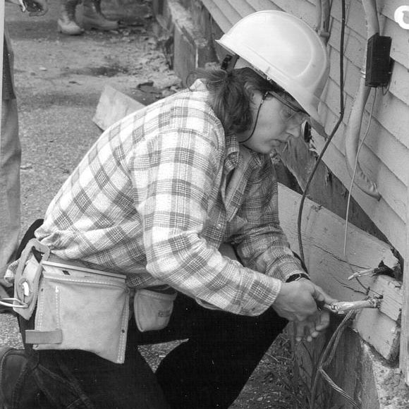 Woman works on outdoor electrical wires. Vermont Works for Women's history dates back to 1987.