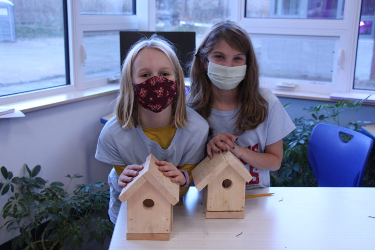 Two campers smile under masks while posing with their birdhouses.