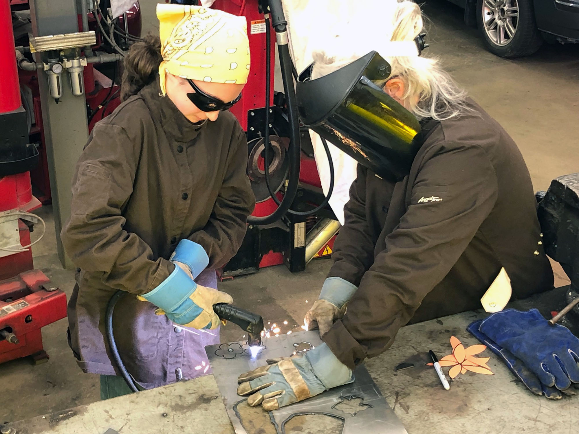 A Rosie’s Girls instructor helps camper use a plasma cutter to make metal flowers.