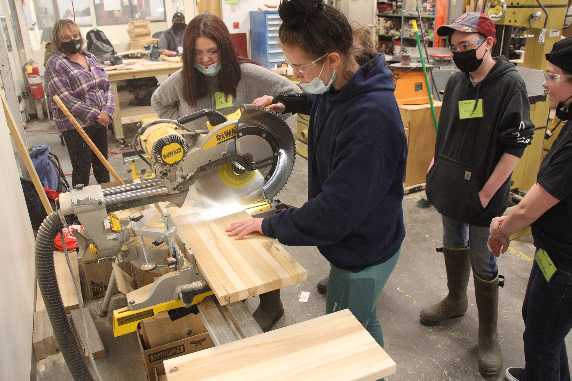 2. A high school student demonstrates for middle school girls how to cut wood using an electric saw.