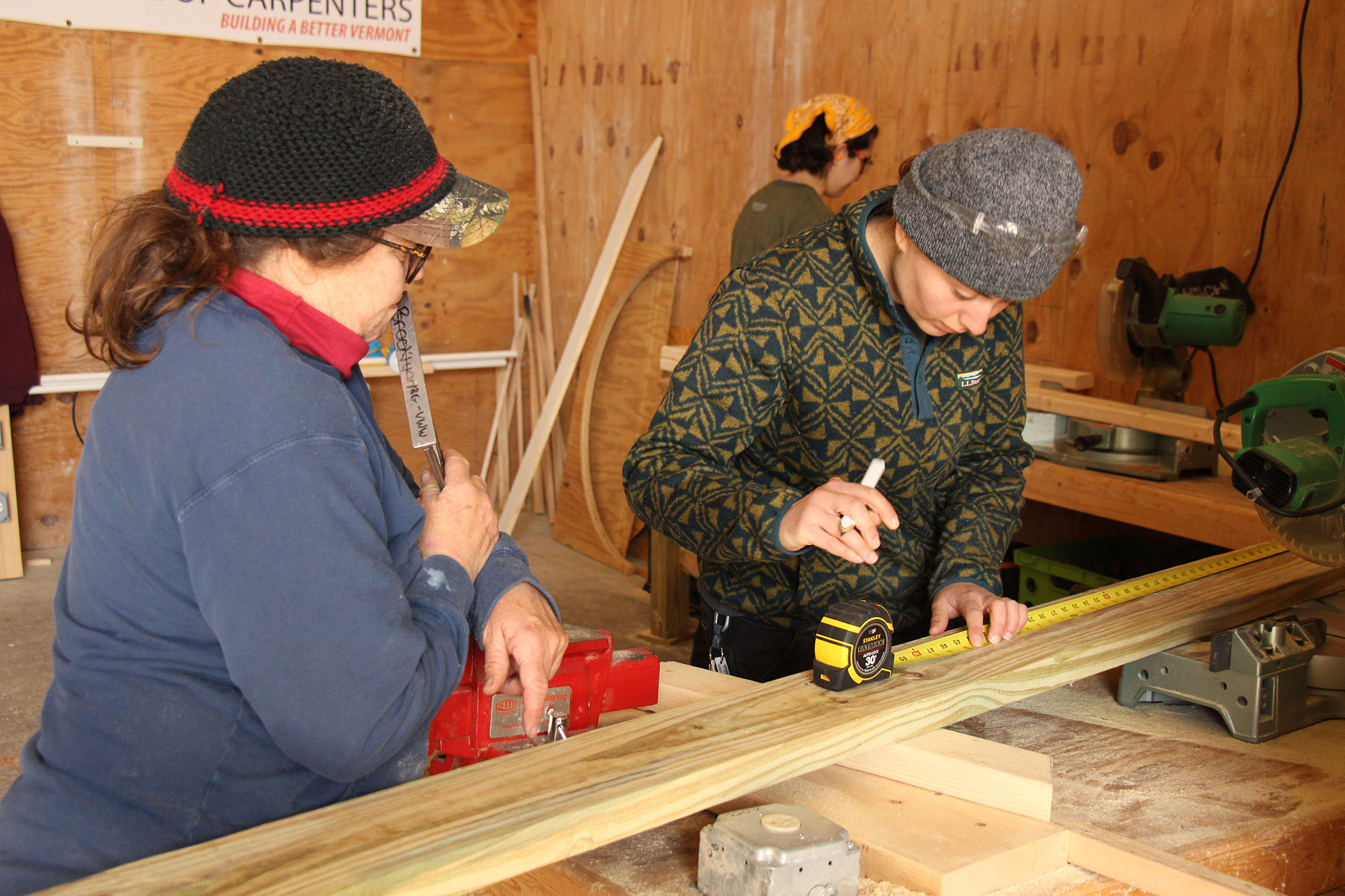 Two trailblazers measure the wood using a tape measure before making a cut with the saw.
