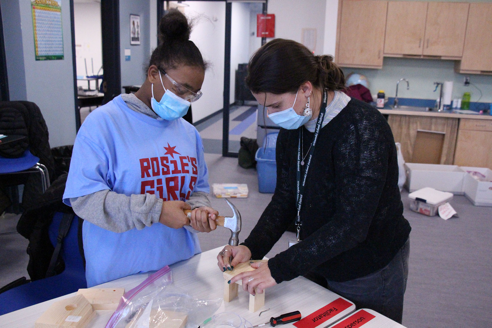 A volunteer instructor assists a middle school student with building a wooden birdhouse.