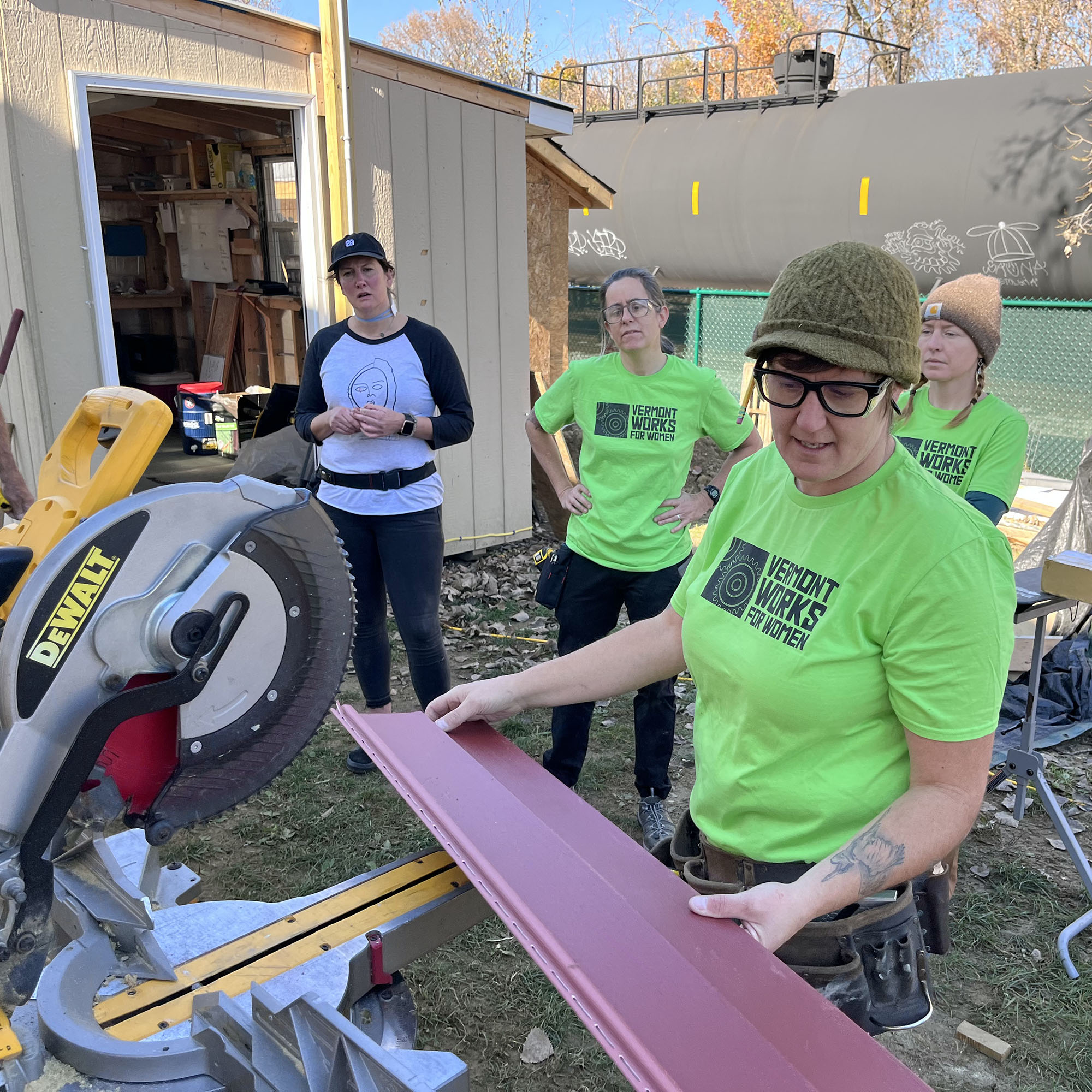 The Trailblazers program instructor places a piece of home siding onto a chop saw outside at a build project. Community impact is part of Trailblazers' program model.
