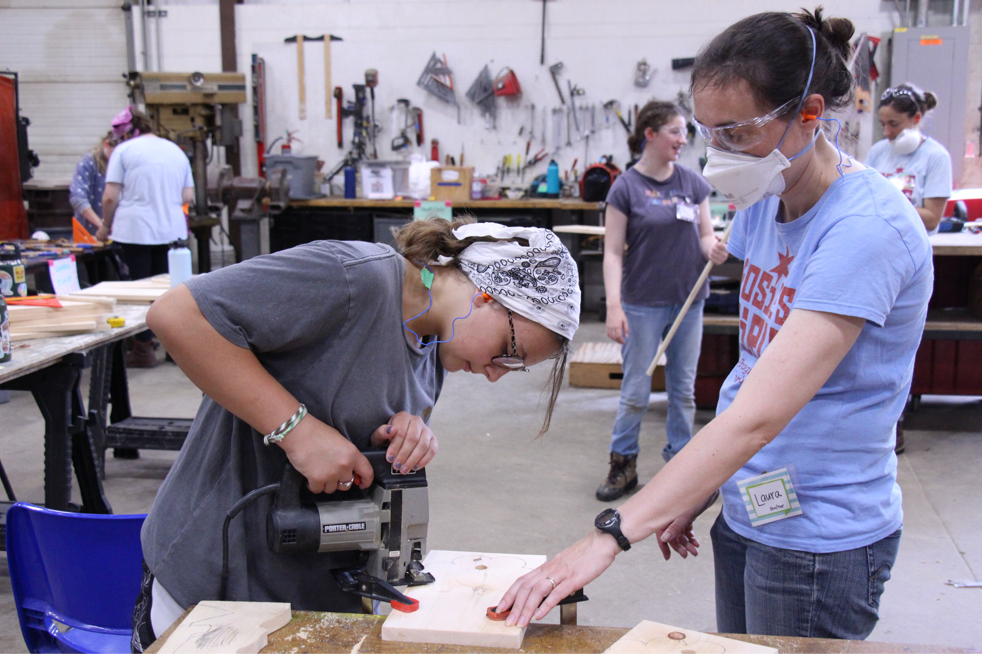 Rosie's Girls camper uses a saw to cut a curve in wood while guided by an instructor