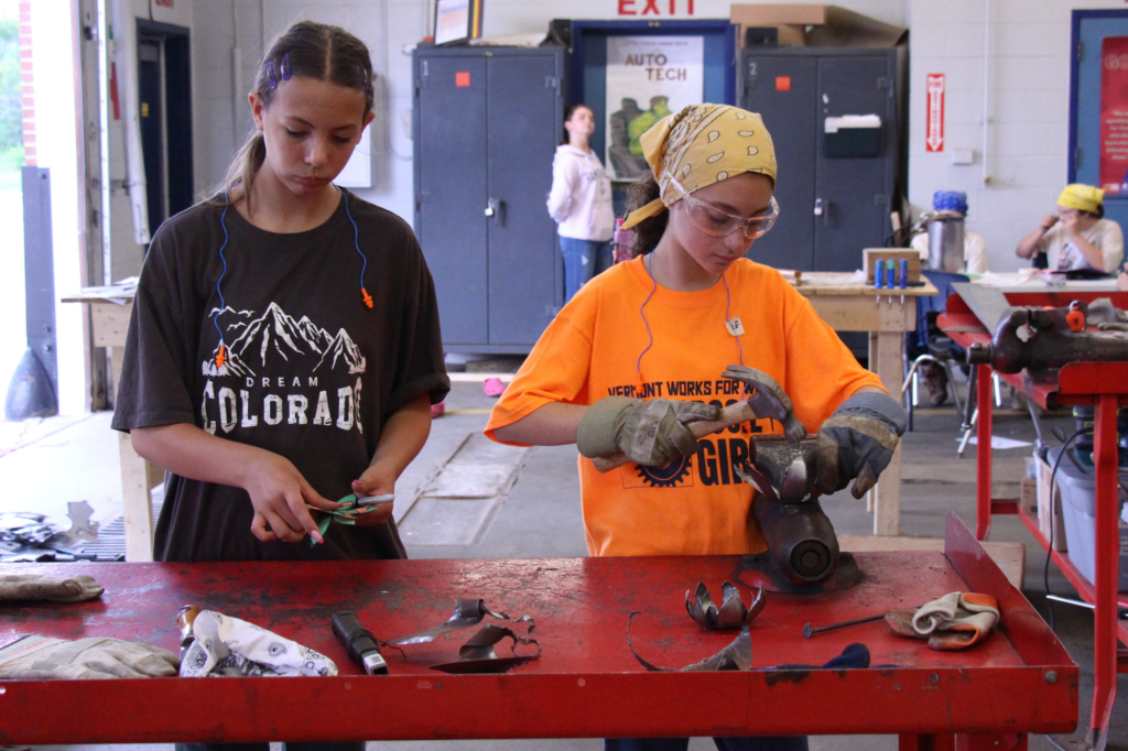 Two Rosie's Girls Campers use hammers to shape and mold metal pieces.