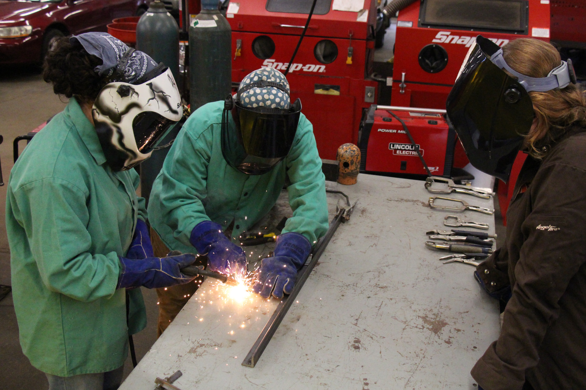 Two campers practice welding as an instructor looks on.