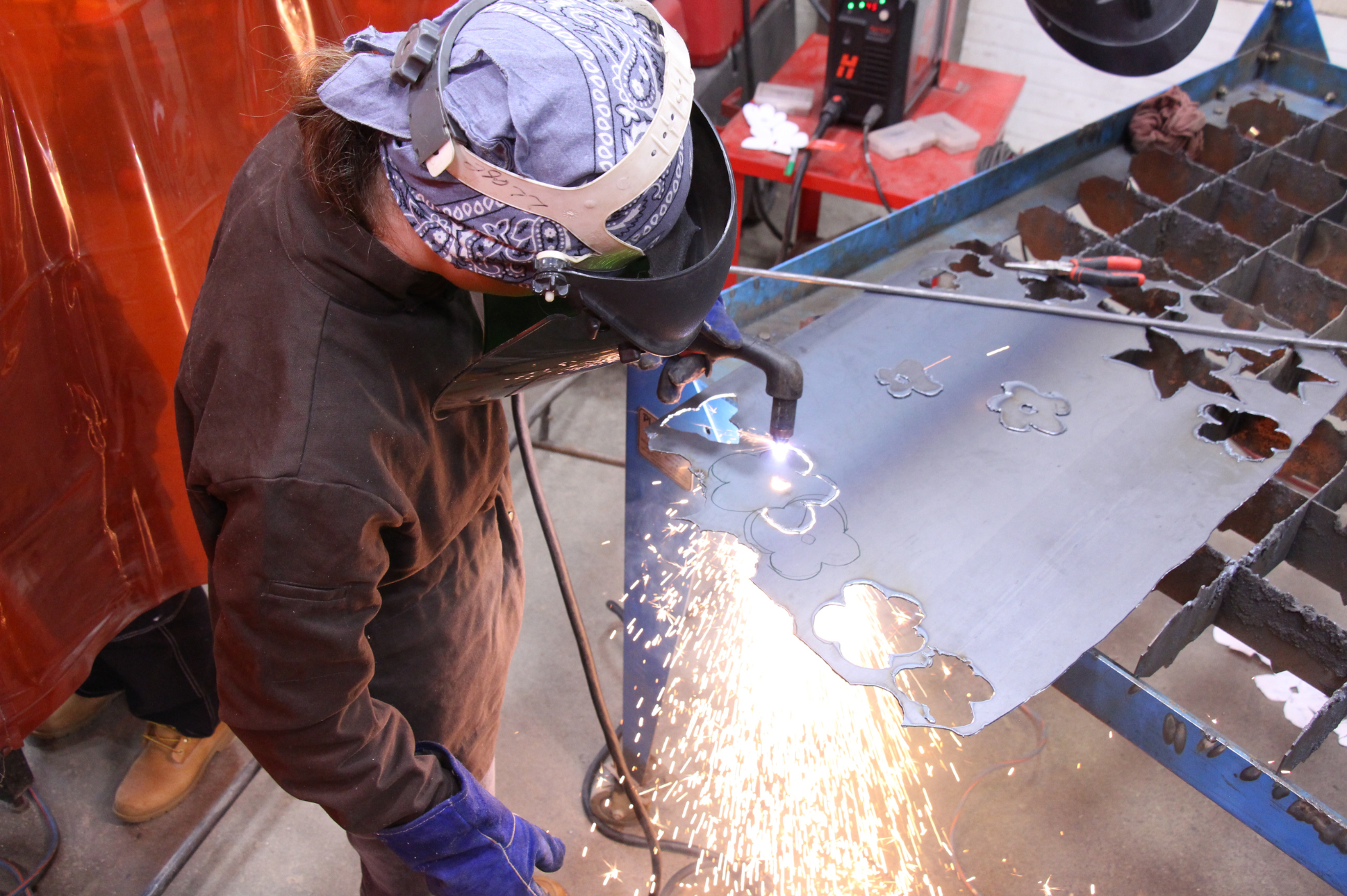 LIFT participant uses a plasma cutter to cut flowers out of sheet metal.
