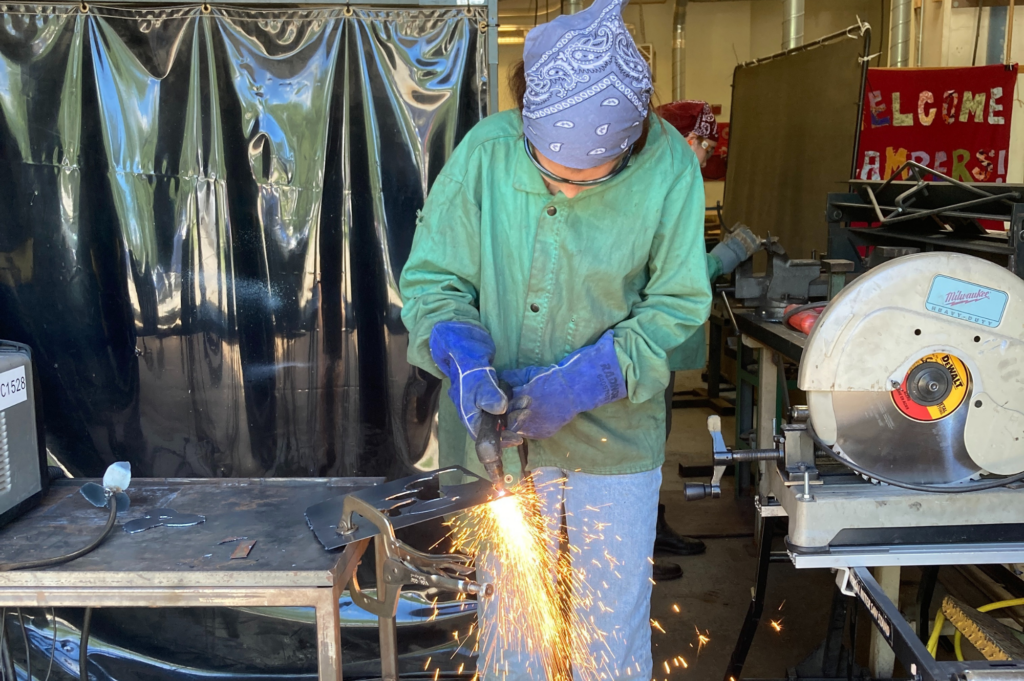 Rosie's Girls camper uses a plasma cutter to cut sheet metal and sparks fly.