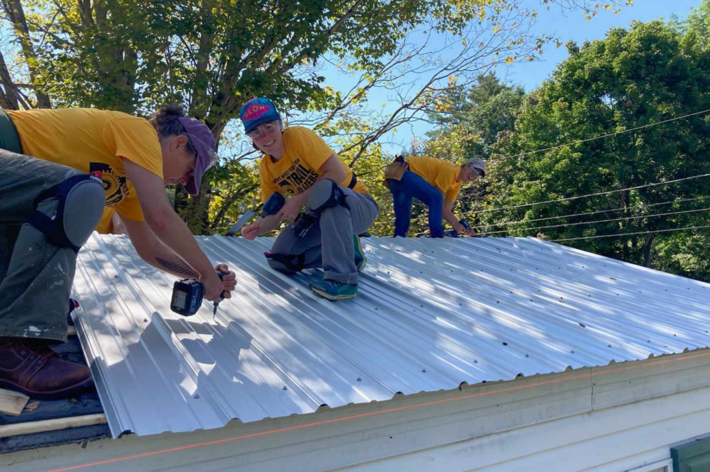 Trailblazers use electric drills to screw metal roofind on to a house.