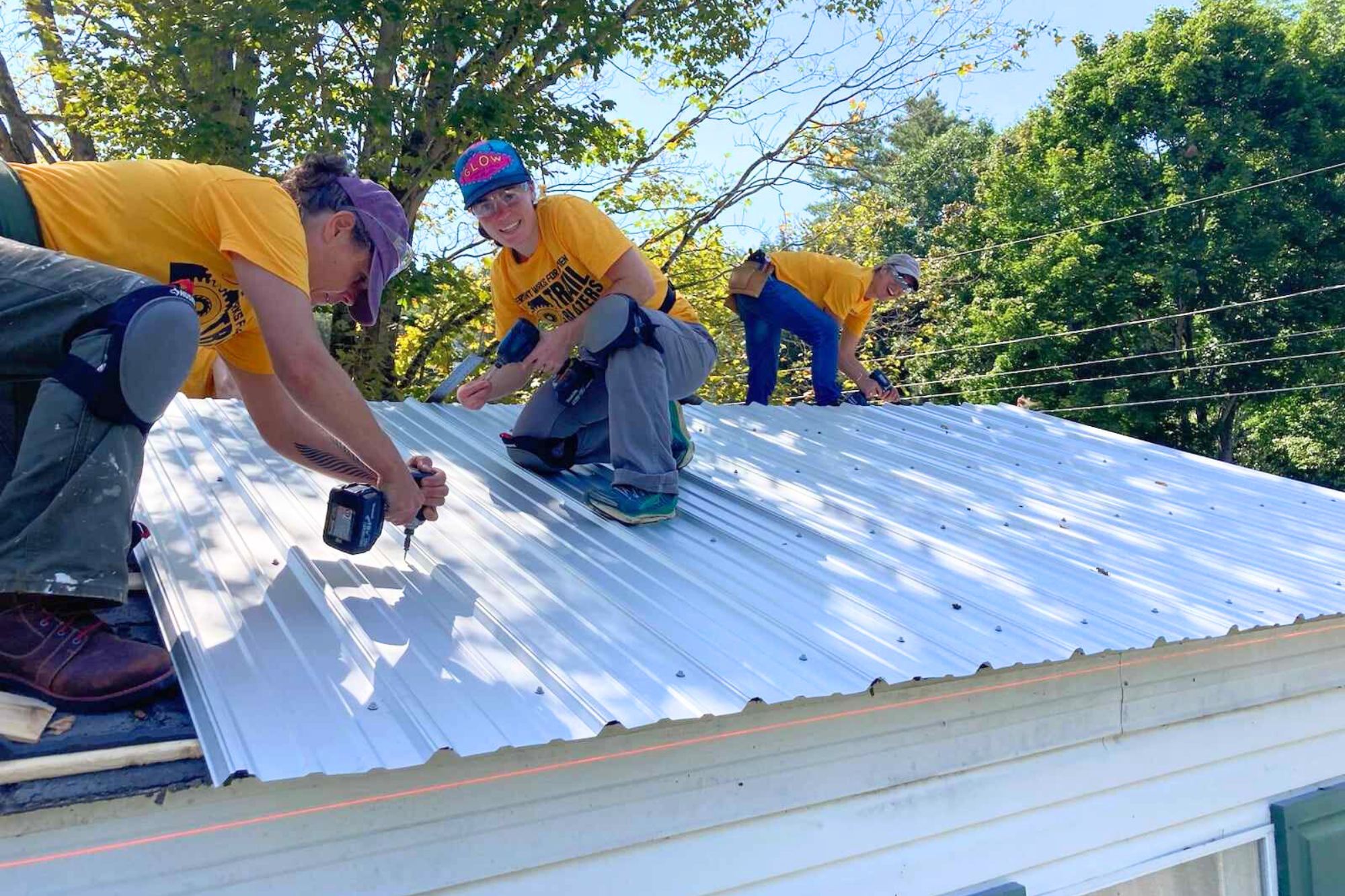 Trailblazers use drills to attached metal roofing on a home.