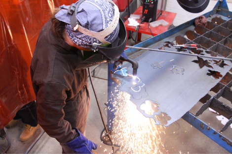 LIFT participant uses a plasma cutter to cut flowers shapes out of sheet metal.