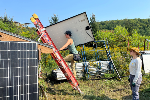 A Trailblazer carries a solar panel up a ladder while the instructor looks on