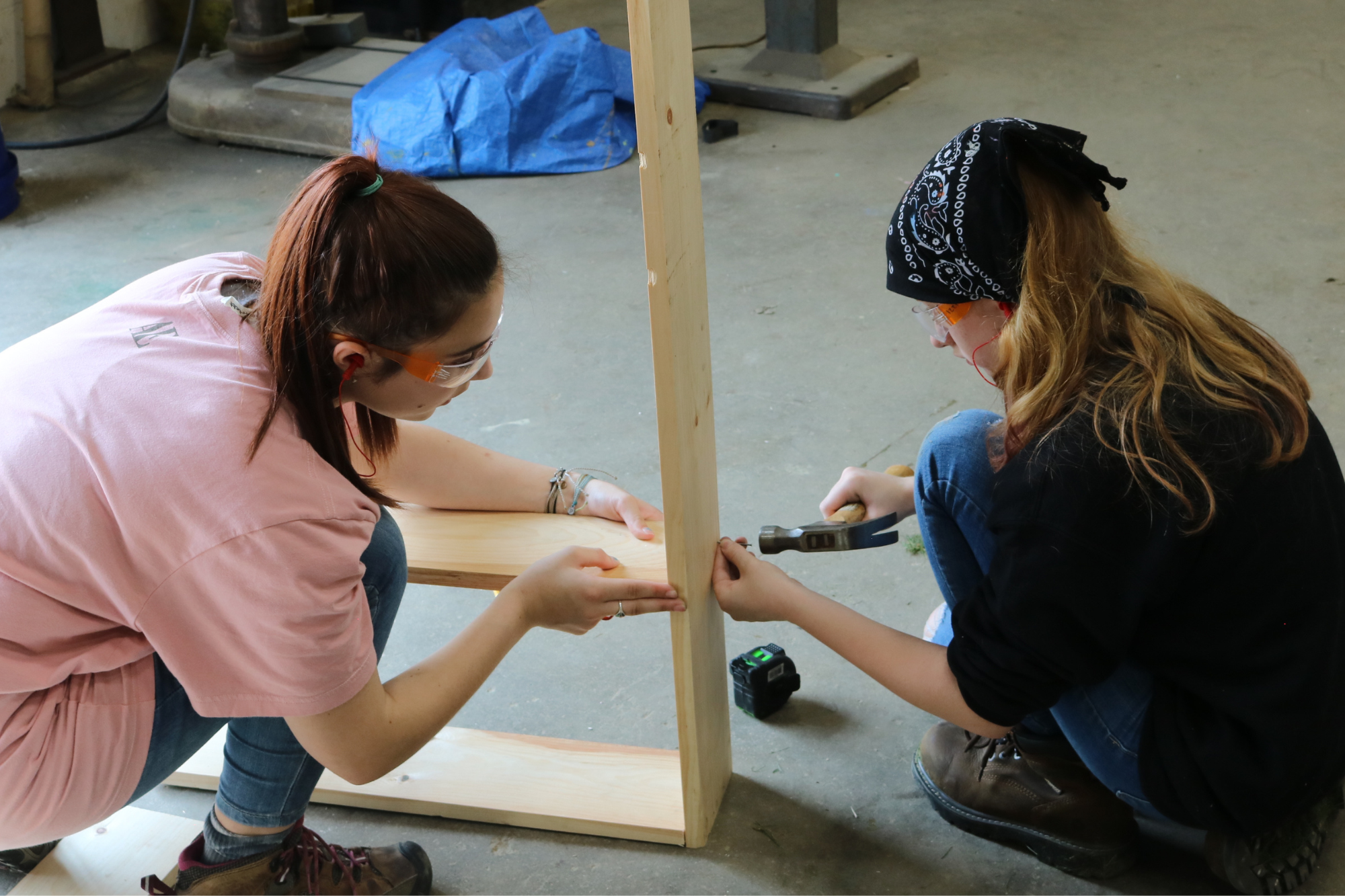 Middle school students uses a hammer at Rosie's Girls Summer camp with help from a CIT.