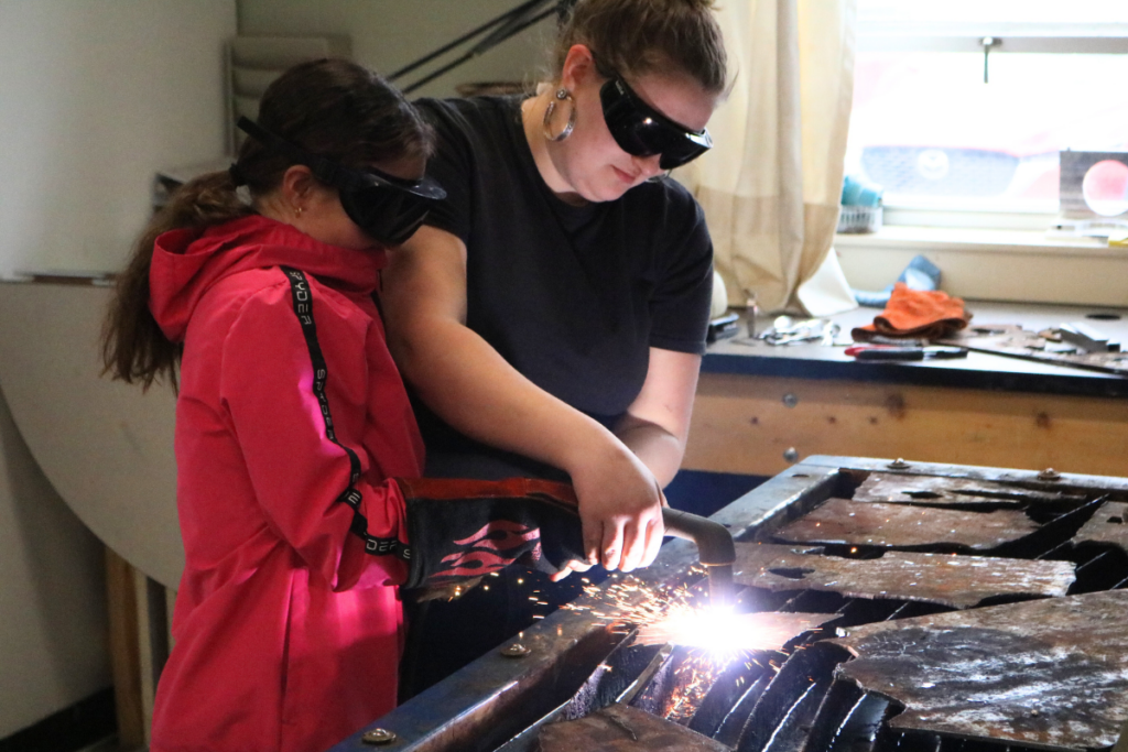 A current tech center student shows a middle school girl how to use a plasma cutter at Career Challenge Day