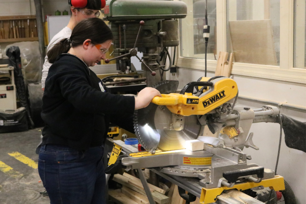 A middle school girl tries using a saw at Career Challenge Day