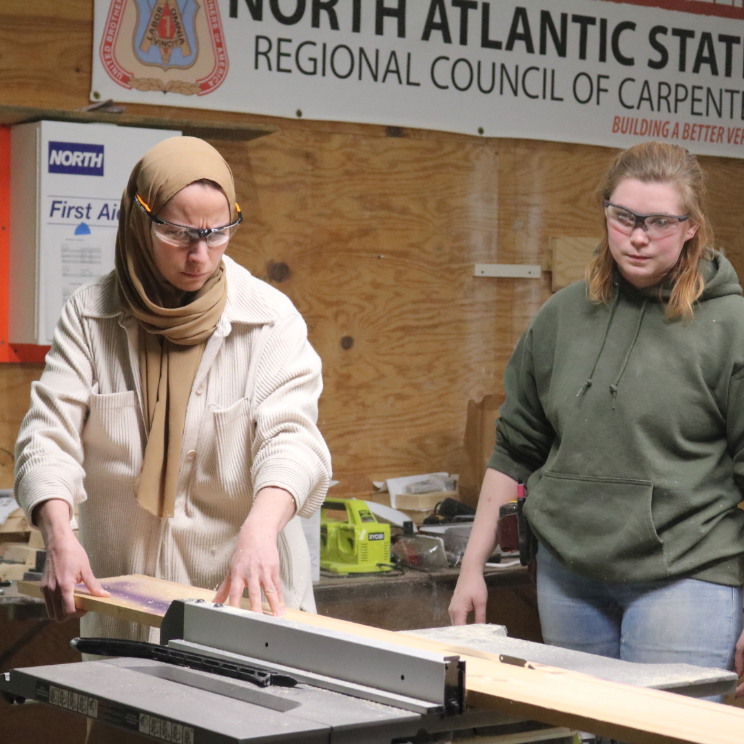 A Trailblazer cuts wood using a table saw while an instructor looks on.