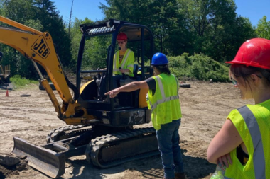 A Trailblazer operates an excavator as an instructor points on. 