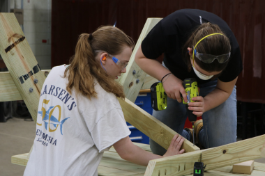 One LIFT participant holds a board while another participant uses a drill to screw.