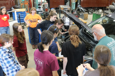 LIFT participants gather around the hood of a car during the automotive lesson