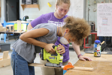 Rosie's Girls camper uses a jigsaw to cut wood at summer camp