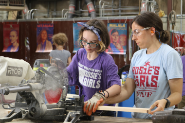 VWW Staffer helps a Rosie's Girls camper use a saw to cut lumber.