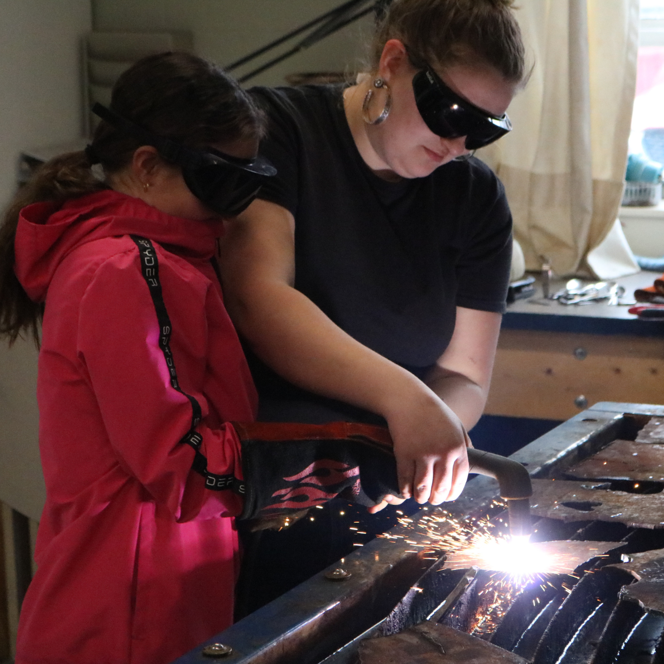 A middle school student uses a plasma cutter with help from a high school student at the tech center