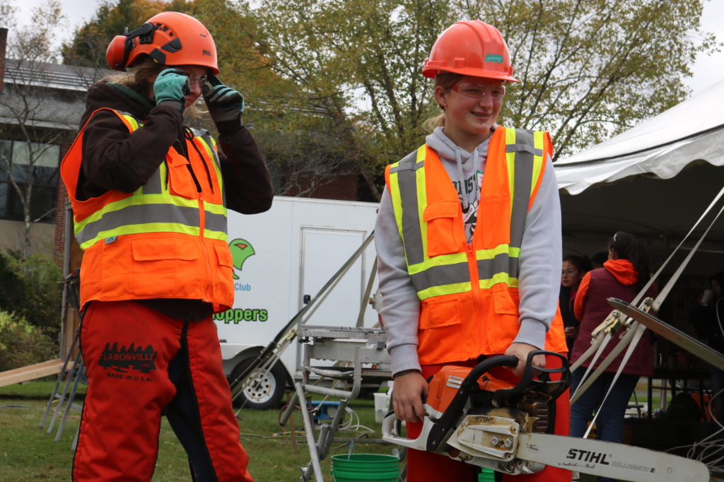 Two students try using a chainsaw at Women Can Do in Randolph.