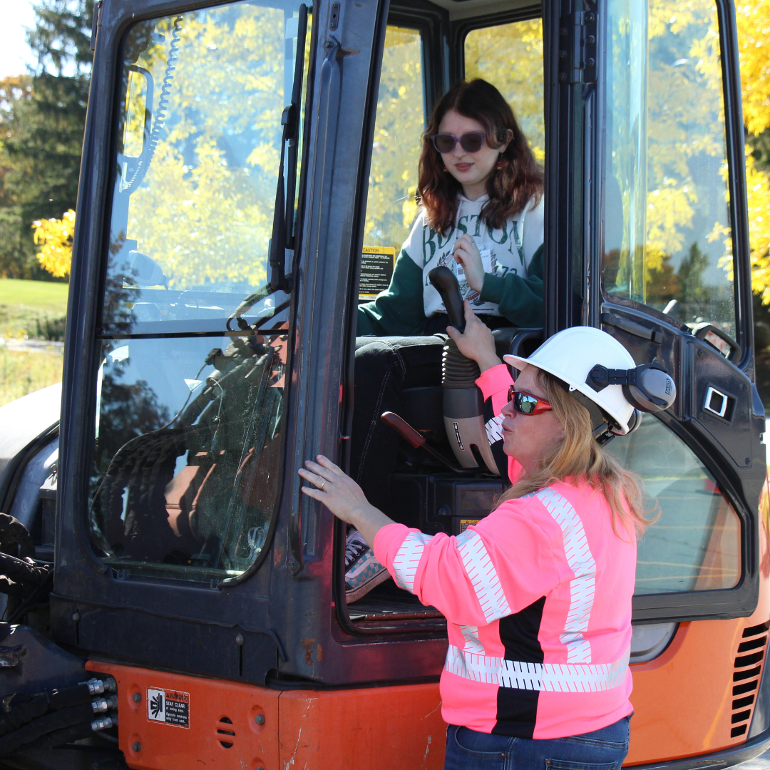 An exhibitor shows a high school student how to use an excavator at Women Can Do
