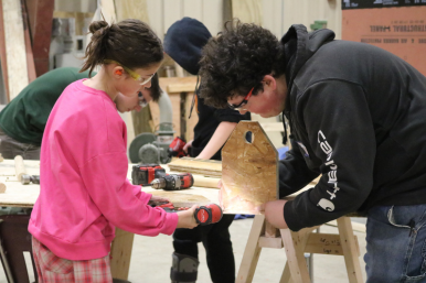 A middle school student uses a drill to build a wooden toolbox at Career Challenge Day