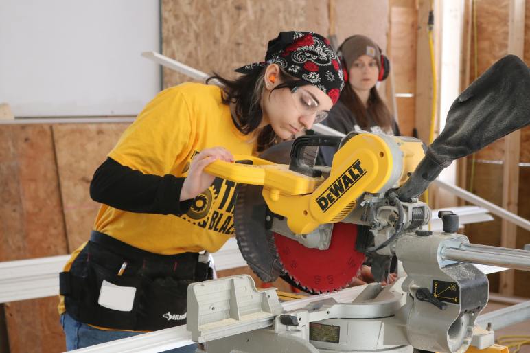 A Trailblazers participant uses a miter saw to cut lumber at Habitat for Humanity
