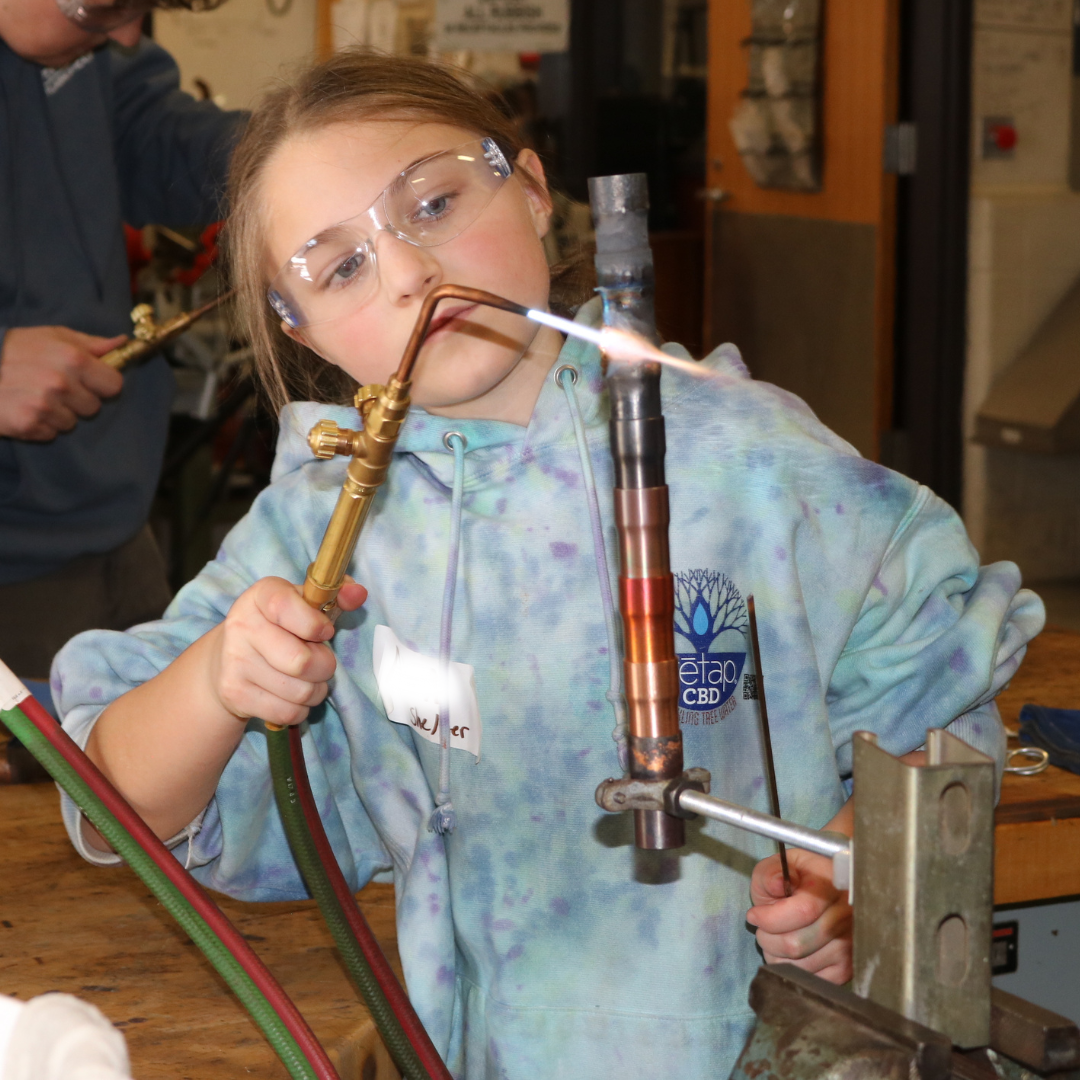 Middle school girls solders copper pipes at Career Challenge Day