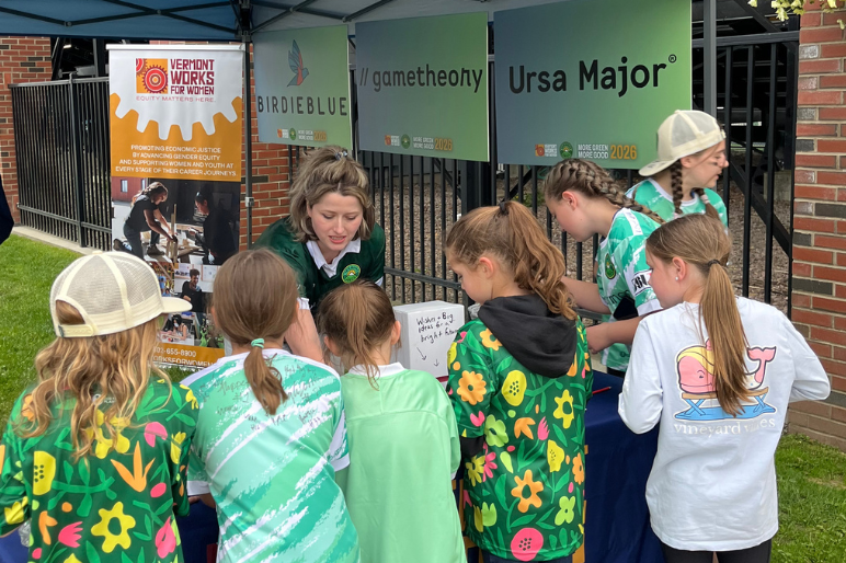 A group of girls gathers at the VWW table to talk with More Green More Good sponsors