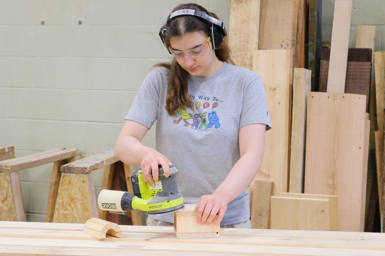 A LIFT participant uses an orbital sander during a carpentry session.