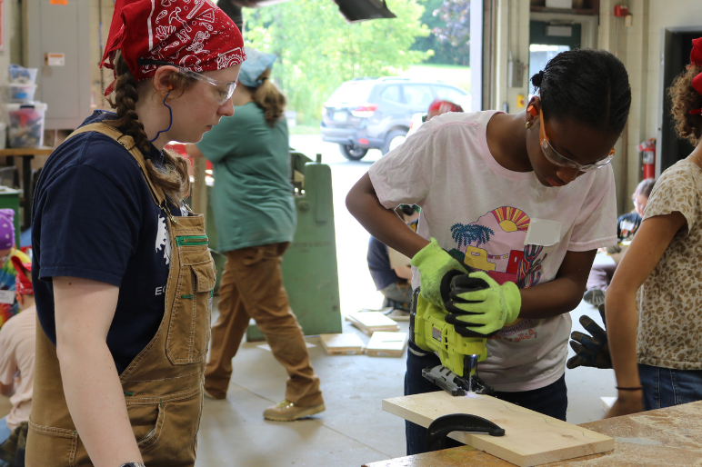 A Rosie's Girls camper uses a jigsaw to cut wood